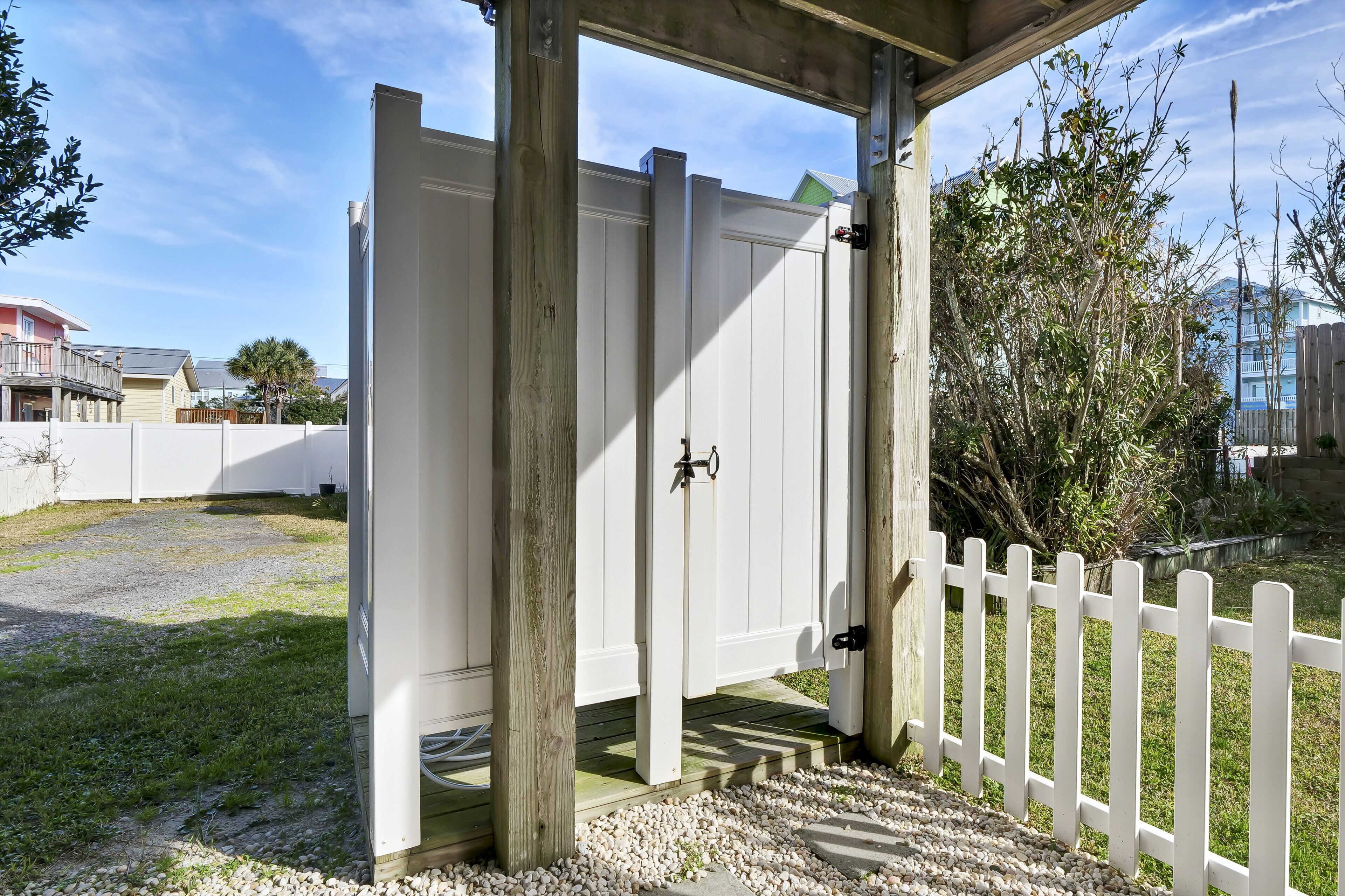 A wooden pergola with a white gate, gravel pathway, and a white picket fence.