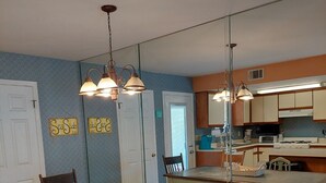 A dining area with a wooden table and chairs, a kitchen in the background, and a patterned rug on the floor. - Great Family Fun On The Emerald Coast In A Gated Resort. (Panama City Beach)