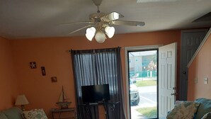 A living room with two sofas, a coffee table, a TV on a stand, a ceiling fan, and a view through a door to the outside. - Great Family Fun On The Emerald Coast In A Gated Resort. (Panama City Beach)