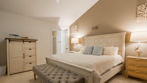 A bedroom with a large bed, a bench, a wardrobe, and a nightstand with a lamp.