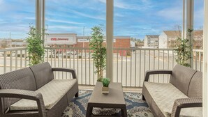 A covered balcony with wicker furniture, a small table, and potted plants.