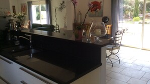 A modern kitchen with a central island, a dining area with a chair, and a view of the outdoors.