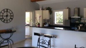 A modern kitchen with wooden beams, a black clock, and a window with a view of trees.