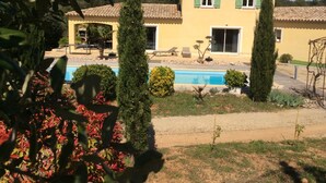 A yellow building with a swimming pool, surrounded by greenery and trees.