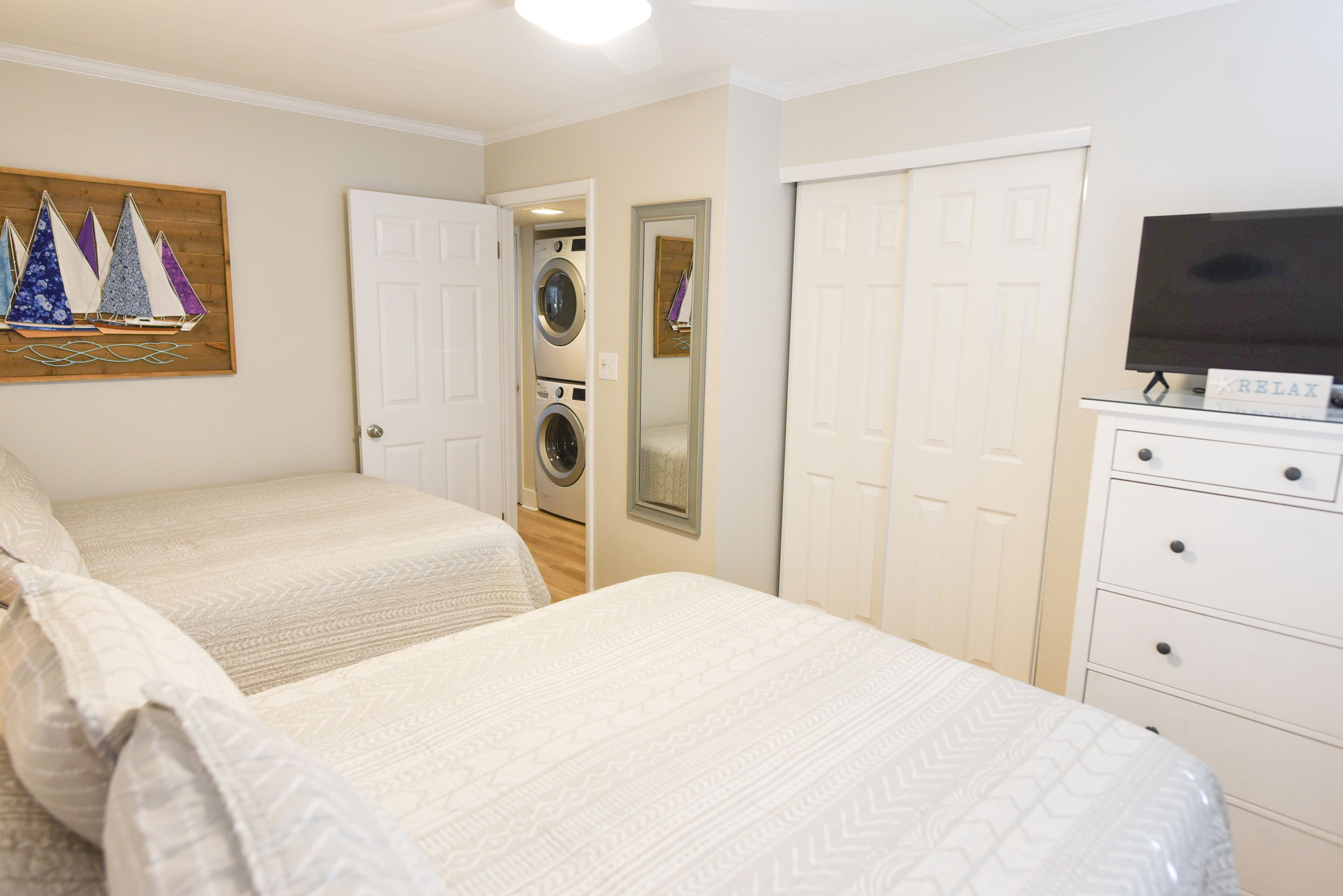 A hotel room with two beds, a washing machine, a mirror, a TV, and a dresser.