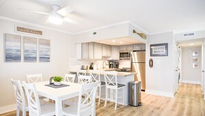 A modern kitchen with white cabinetry, a stainless steel refrigerator, and a dining area with white chairs and a table. - Direct Ocean Front Building, Oceanview, Mid-Town 39th St, First Floor Unit  (Ocean City)