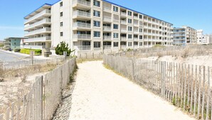A multi-story hotel with balconies, a sandy path leading to the entrance, and a wooden fence. - Direct Ocean Front Building, Oceanview, Mid-Town 39th St, First Floor Unit  (Ocean City)
