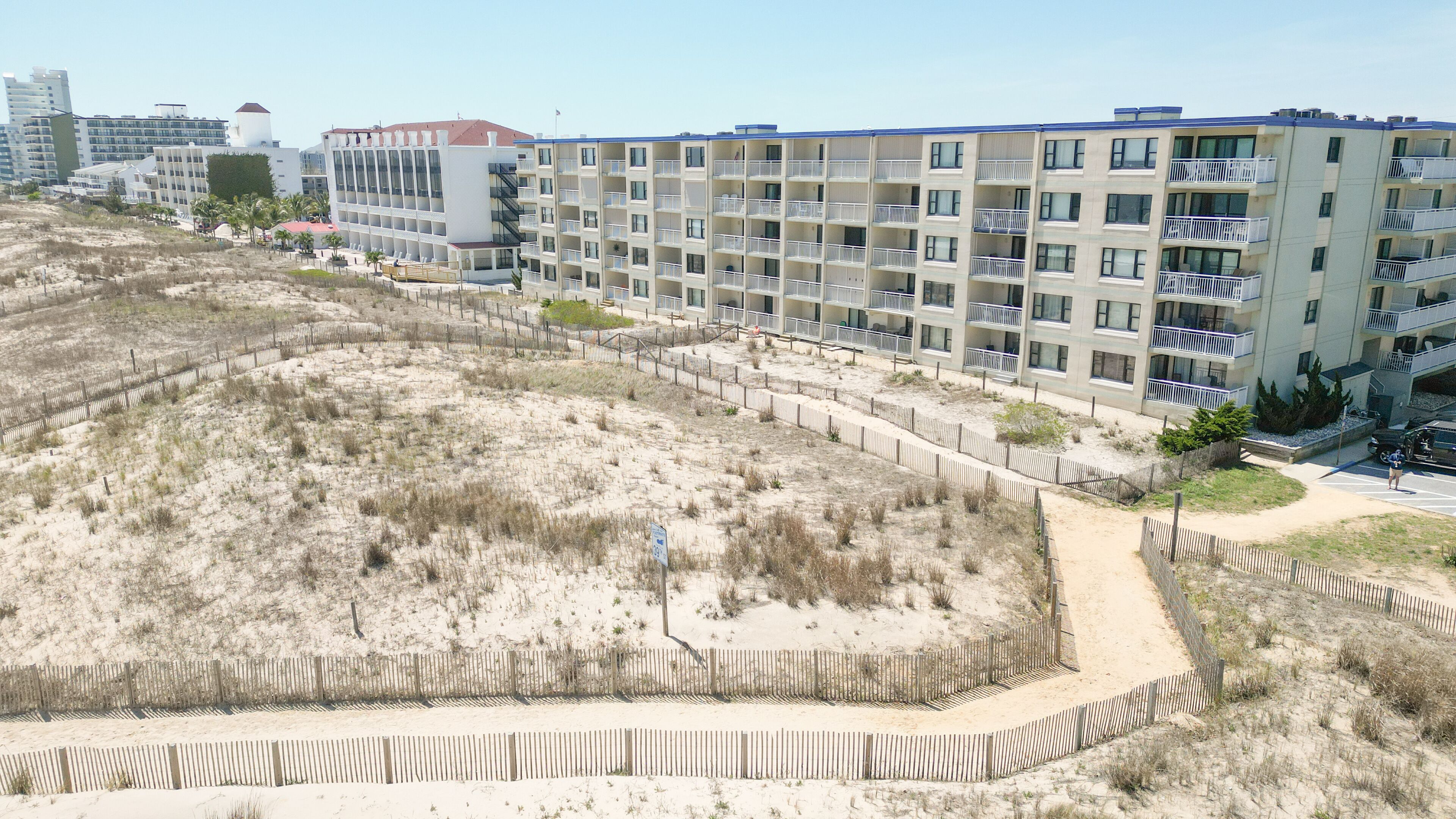 A beachfront hotel with multiple balconies, a sandy beach area, and a fenced walkway.