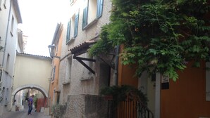 Une ruelle étroite pavée de pierres, bordée de bâtiments des deux côtés, avec une arche en pierre et un escalier menant à une porte.