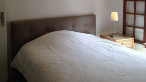 Une chambre à coucher avec un grand lit, une table de chevet avec une lampe et une fenêtre à vitres dépolies.