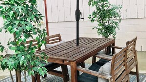 A wooden table with a red umbrella, surrounded by chairs and potted plants.