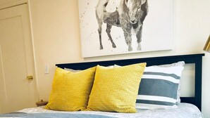 A bed with a white and blue striped bedspread, two yellow pillows, and a gray and white striped pillow.