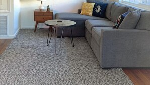 A living room with a grey sectional sofa, a small round coffee table, a side table, and a large abstract painting on the wall.