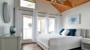 Un dormitorio con una cama grande, un ventilador de techo, una ventana con cortinas y una obra de arte colgada en la pared.