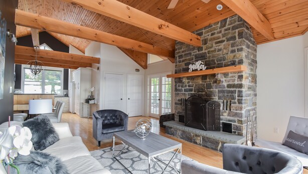 Un salón espacioso con chimenea de piedra, vigas de madera y muebles modernos.