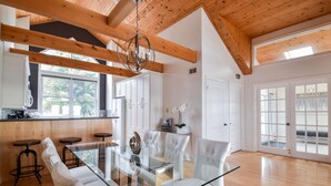 Una cocina moderna con vigas de madera, armarios blancos y una mesa de comedor de vidrio.