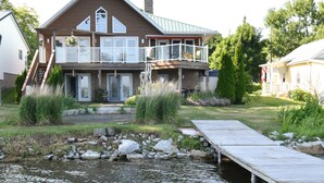 Una casa de dos pisos con un balcón, un muelle que se adentra en un estanque y un jardín bien cuidado.