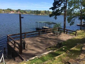 Um deck de madeira com uma mesa e cadeiras, com vista para um lago com um píer e uma área de estar coberta.