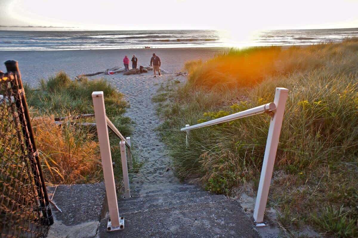 Un sentier menant à une plage, avec une rambarde sur un côté.
