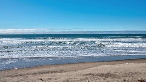 Une plage avec des vagues, un ciel dégagé et des montagnes à l’horizon.