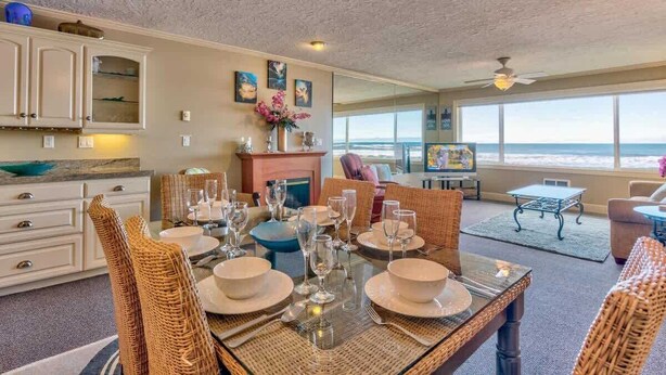 Un coin repas avec une table dressée pour six personnes, une cuisine avec des meubles blancs et une vue sur l’océan.