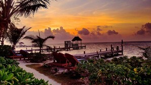 A beachside resort with a wooden pier, lounge chairs, and a thatched hut. - Sea Front Property - "Sea Turtle" pool/bikes included/tours! (San Pedro)