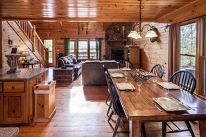A wooden cabin interior with a dining area, kitchen, and living room.