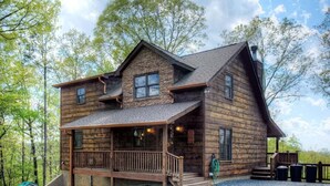 Uma cabana rústica de toras com varanda, chaminé e um pequeno deck.