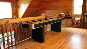 Interior de madeira com mesa de bilhar, uma janela com cortinas e uma parede de pedra.