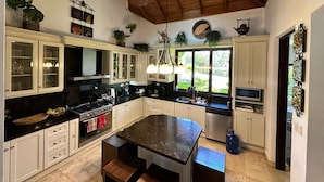 Una cocina con armarios blancos, una isla con encimera de granito, una estufa y un ventilador de techo.