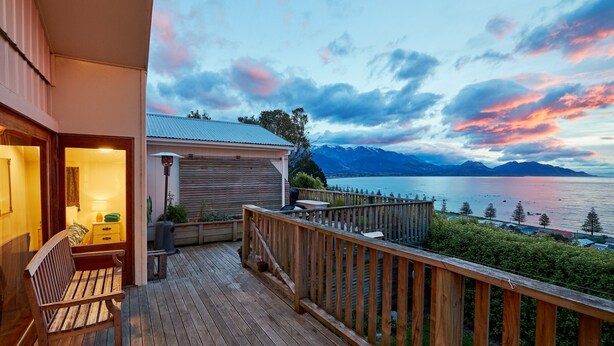 A wooden deck with a bench, a small table, and a lamp. - Three bedroom cottage with stunning panoramic views of the sea and mountains. (Kaikoura)