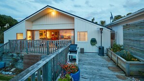 A modern house with a large deck, a covered patio, and a well-lit interior. - Three bedroom cottage with stunning panoramic views of the sea and mountains. (Kaikoura)
