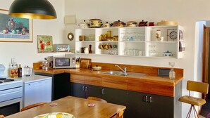 A modern kitchen with wooden cabinets, a built-in microwave, and a sink. There is a dining table with chairs and a pendant light above. - Three bedroom cottage with stunning panoramic views of the sea and mountains. (Kaikoura)