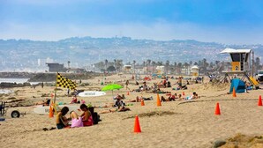 Ein Strand mit Rettungstürmen, Sonnenschirmen und entspannten Menschen.