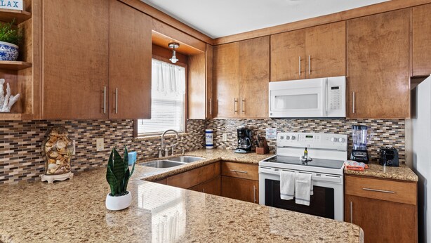 A kitchen with wooden cabinets, granite countertops, a microwave, stove, and a sink.