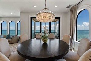 A dining area with a chandelier, round table, and chairs, overlooking a scenic ocean view. - Serendipity Deux: Luxury Beachfront Retreat + Elevator + Complimentary Golf Cart (Anna Maria)