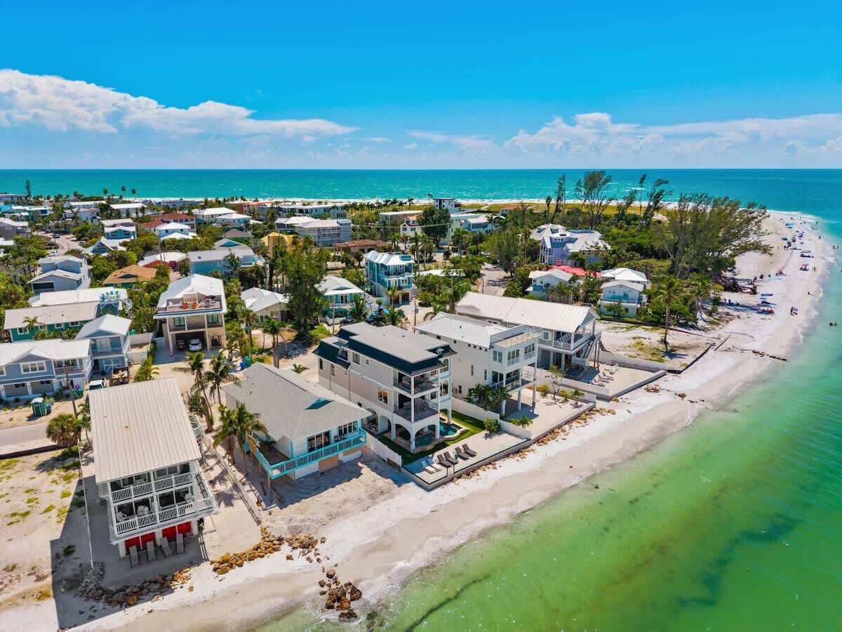 A coastal residential area with beachfront properties, including multi-story houses and villas, some with balconies and pool areas.