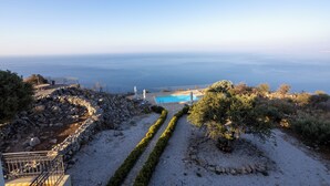 Zona de piscina con vista despejada al mar, rodeada por un muro de piedra y un camino.