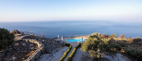 A pool area with a clear view of the sea, surrounded by a stone wall and a pathway.