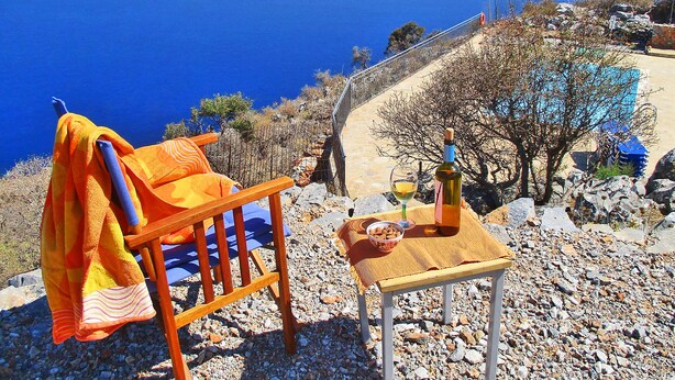 Una silla con una toalla, una botella de vino y una copa sobre una mesa con vista al mar y a las montañas.