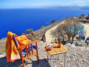 Una silla con una toalla, una botella de vino y una copa sobre una mesa con vista al mar y a las montañas.