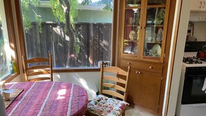 A kitchen with a dining area, a window with a view of a backyard, and a cabinet with glass doors. - Peaceful Escape, Tropical Gardens, Easy Walk to Beach & Eats  (Capitola)