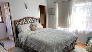 A neatly made bed with a patterned bedspread and pillows, a wooden headboard, a small rug, and a window with sheer curtains. - Peaceful Escape, Tropical Gardens, Easy Walk to Beach & Eats  (Capitola)