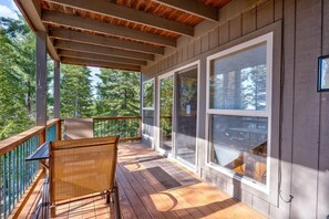 A covered porch with a wooden bench, large windows, and a view of trees. - Falcons Nest (Downstairs) (Yosemite National Park)