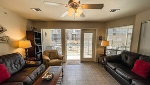 A living room with two leather sofas, a coffee table, a ceiling fan, and a view through a glass door to an outdoor patio. - Country Cousins | Pet-Friendly | 1st Floor | Pool (New Braunfels)