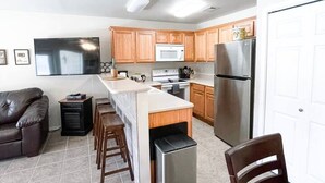 A modern kitchen with wooden cabinets, a stainless steel refrigerator, a microwave, and a built-in island with bar stools. - Country Cousins | Pet-Friendly | 1st Floor | Pool (New Braunfels)