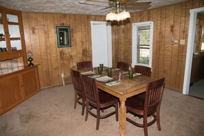 Une salle à manger avec une table et des chaises en bois, un lustre et un miroir au mur.