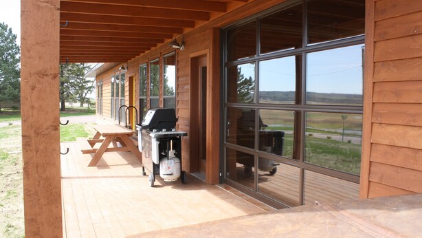 Un espacio exterior cubierto con una parrilla y una mesa, ventanas amplias y vistas al paisaje.