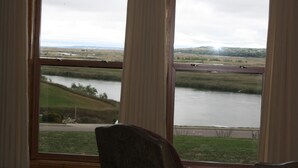 Una habitación con un ventanal grande que da a un lago, una carretera y colinas distantes.