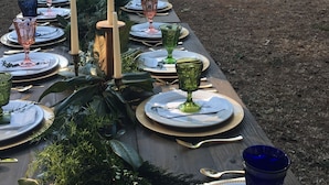 Uma longa mesa de jantar posta ao ar livre, com várias velas e copos.